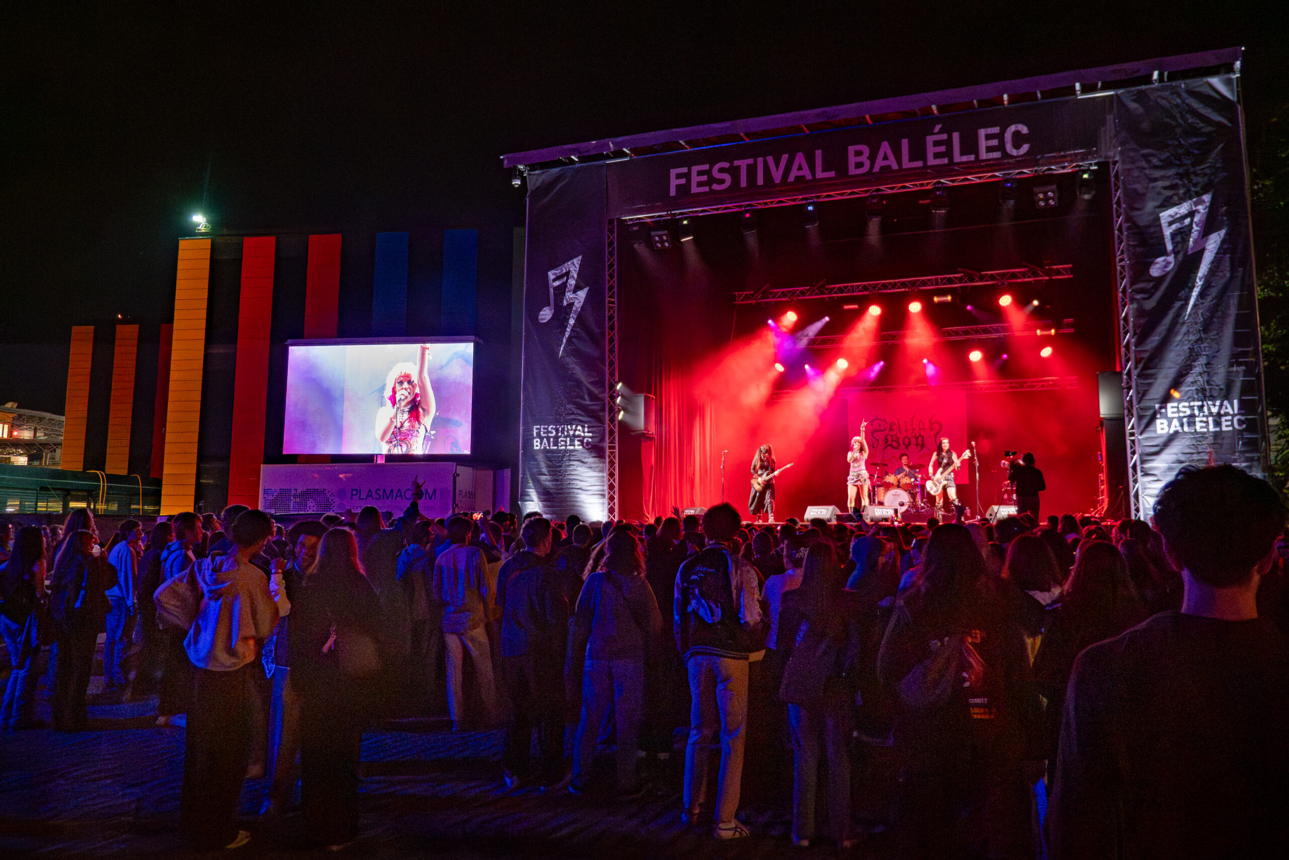 Une masse de personnes devant une scène sur laquelle se déroule un concert, avec un écran géant sur la gauche. Une masse de personnes devant une scène sur laquelle se déroule un concert, avec un écran géant sur la gauche.